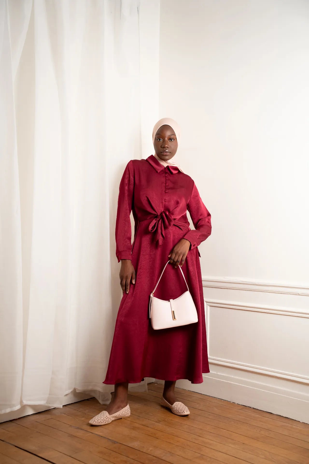 Robe longue satinée rouge bordeaux nouée à la taille avec hijab et sac à main beige