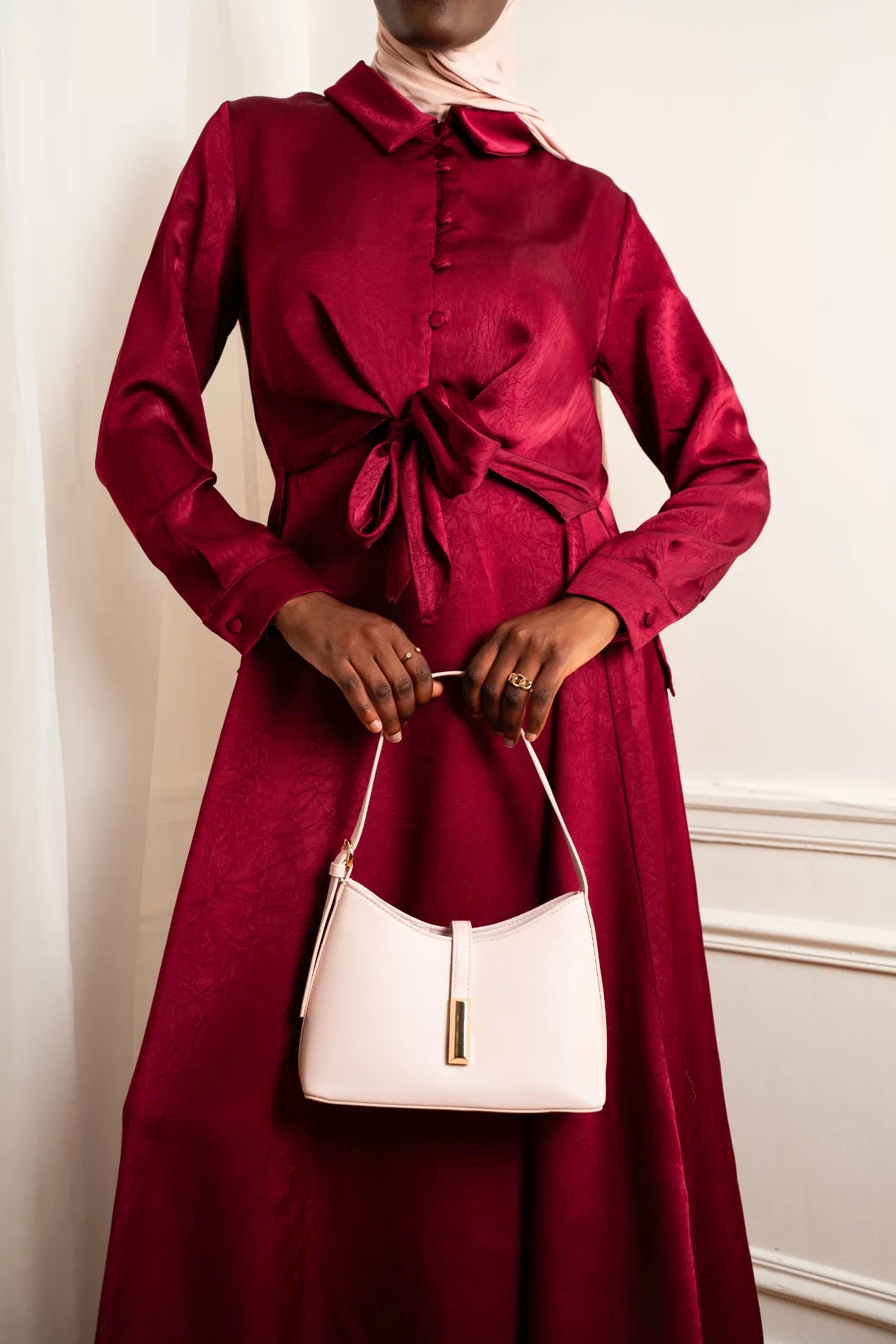Gros plan sur une robe longue satinée rouge bordeaux et sac à main beige