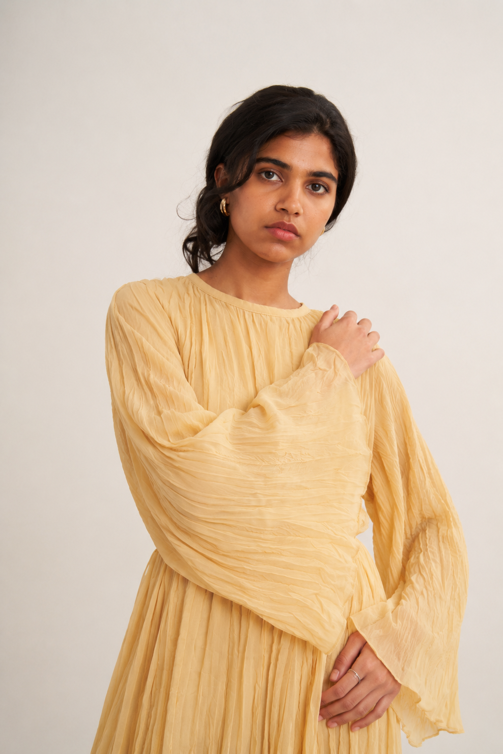 Gros plan sur une robe longue plissée jaune beige à manches évasées