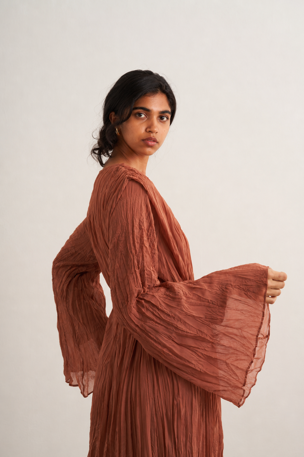 Gros plan sur une robe longue plissée terracotta à manches évasées